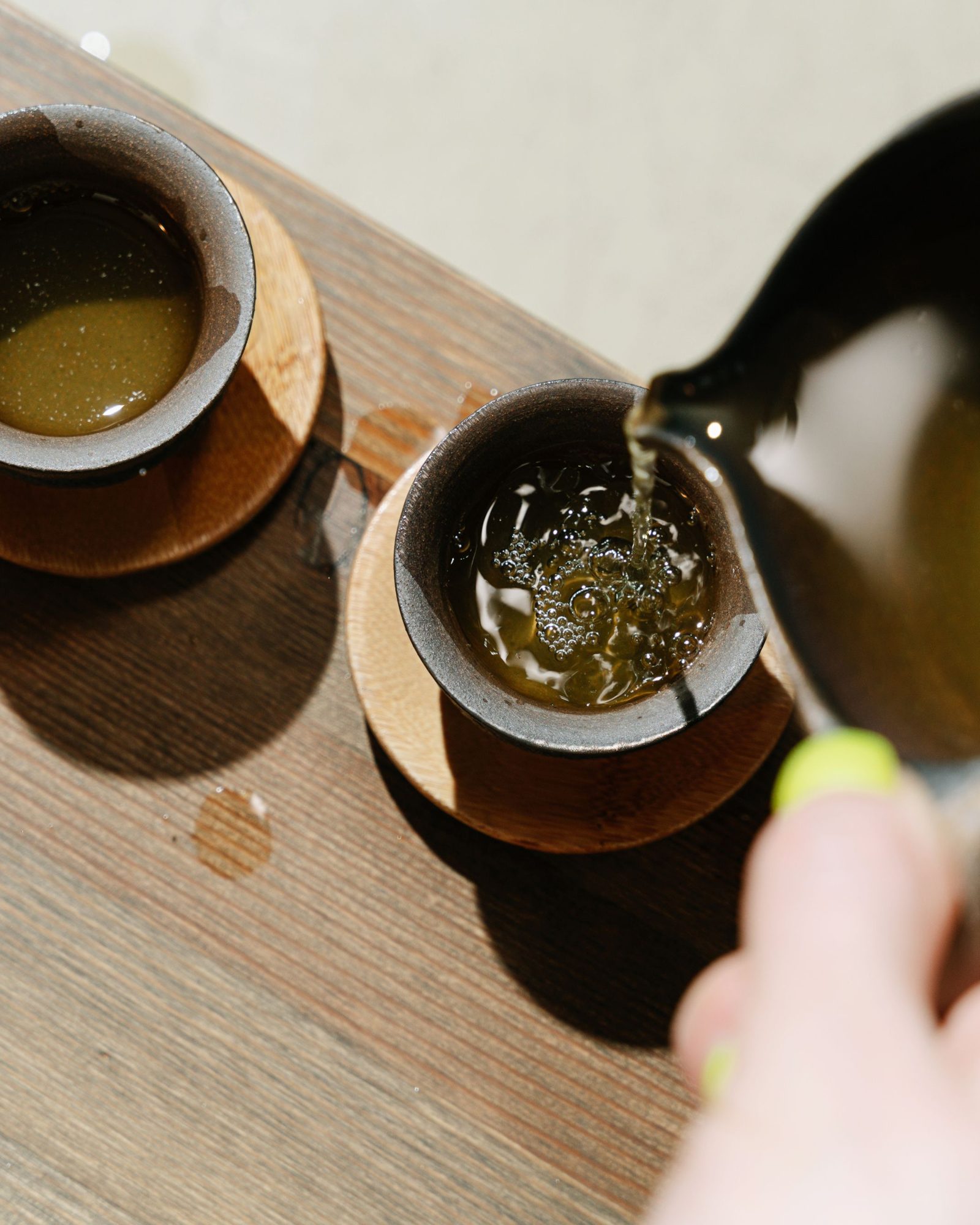 Mains versant une infusion de plantes dans une tasse en céramique, sur une table en bois clair